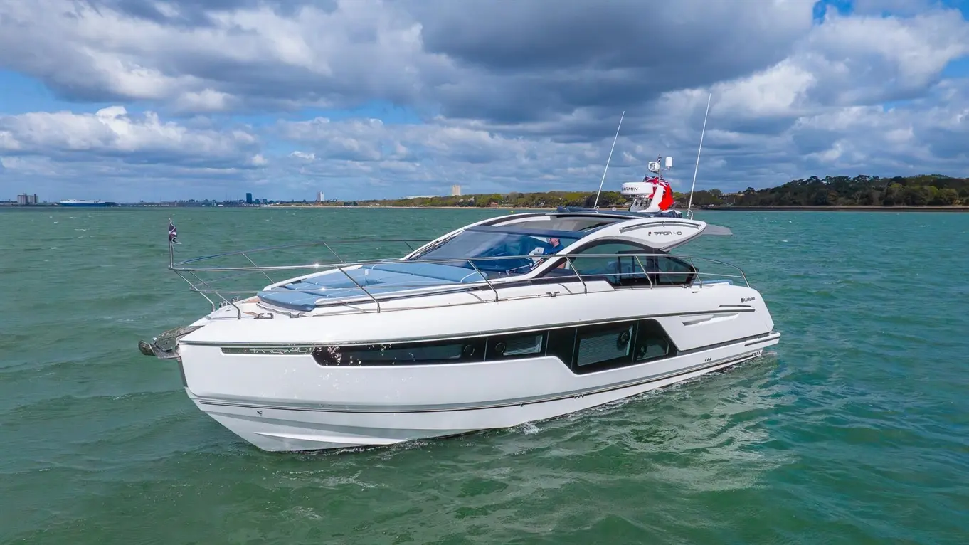 White luxury motorboat cruising on green water under a partly cloudy sky, with a skyline visible in the background.